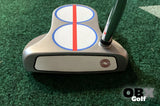 A golf putter with a red center line sticker on the head on the green.