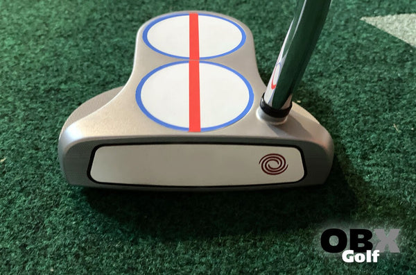 A golf putter with a red center line sticker on the head on the green.